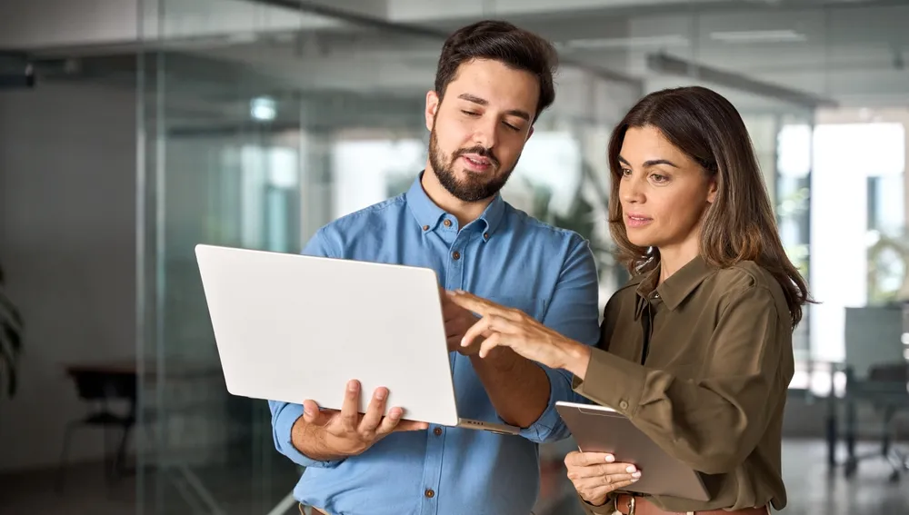 Two colleagues reviewing plans on a laptop and tablet